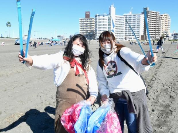 two women picking up trash on the beach