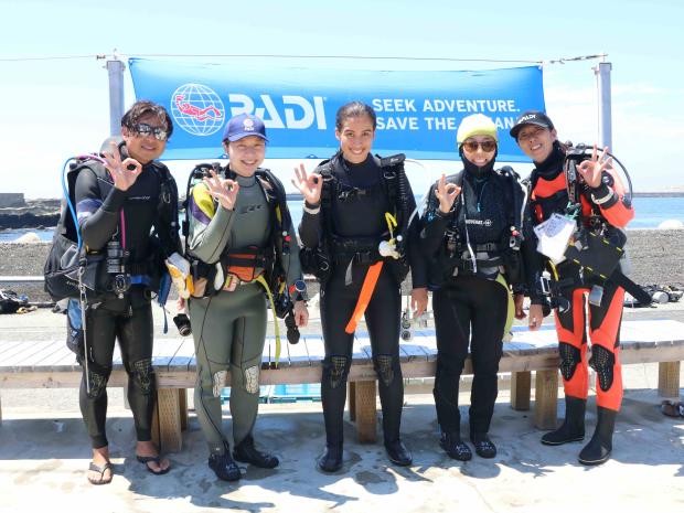 3 student divers and 2 instuctors posing behind PADI banner