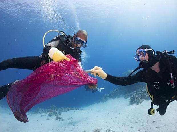 two divers holding a trash bag underwater