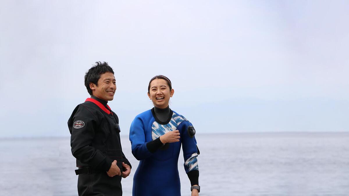 海辺でドライスーツを着て談笑するダイバー